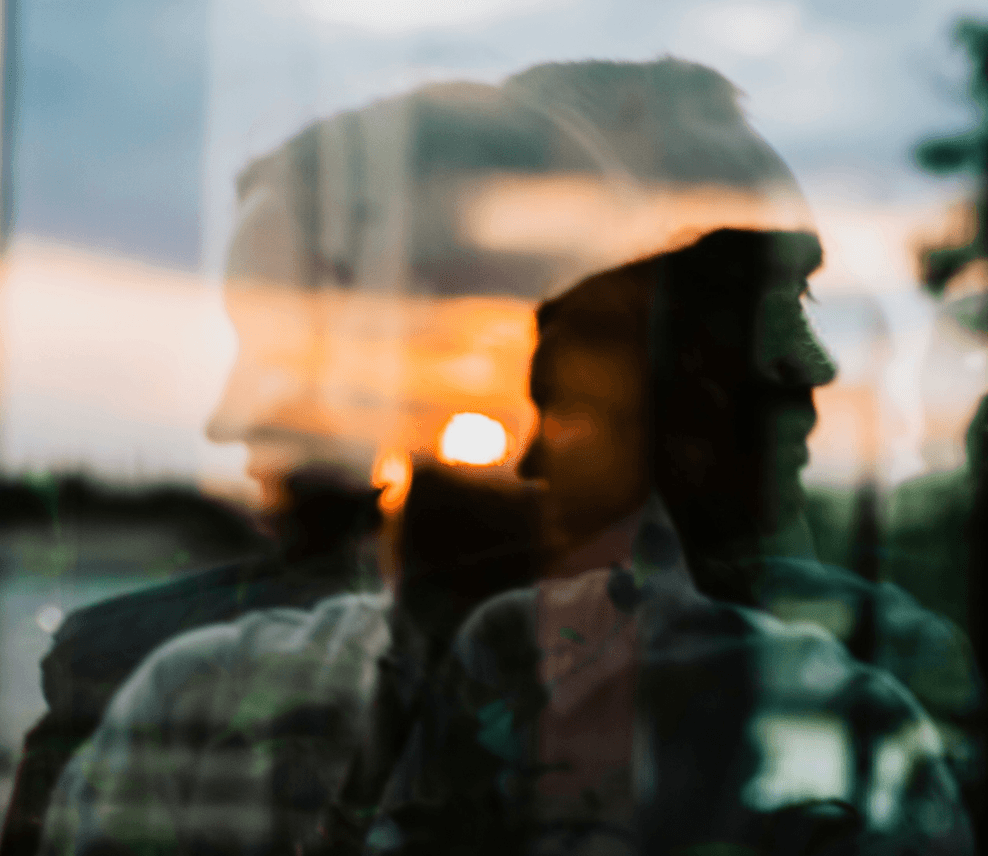 Double-exposure portrait of a man's silhouette against a sunset reflected in glass